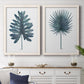 Set of two white barnwood framed canvas prints depicting a coordinated art pair of large blue-green tropical leaves rendered as modern botanical illustrations above a dining room sideboard.