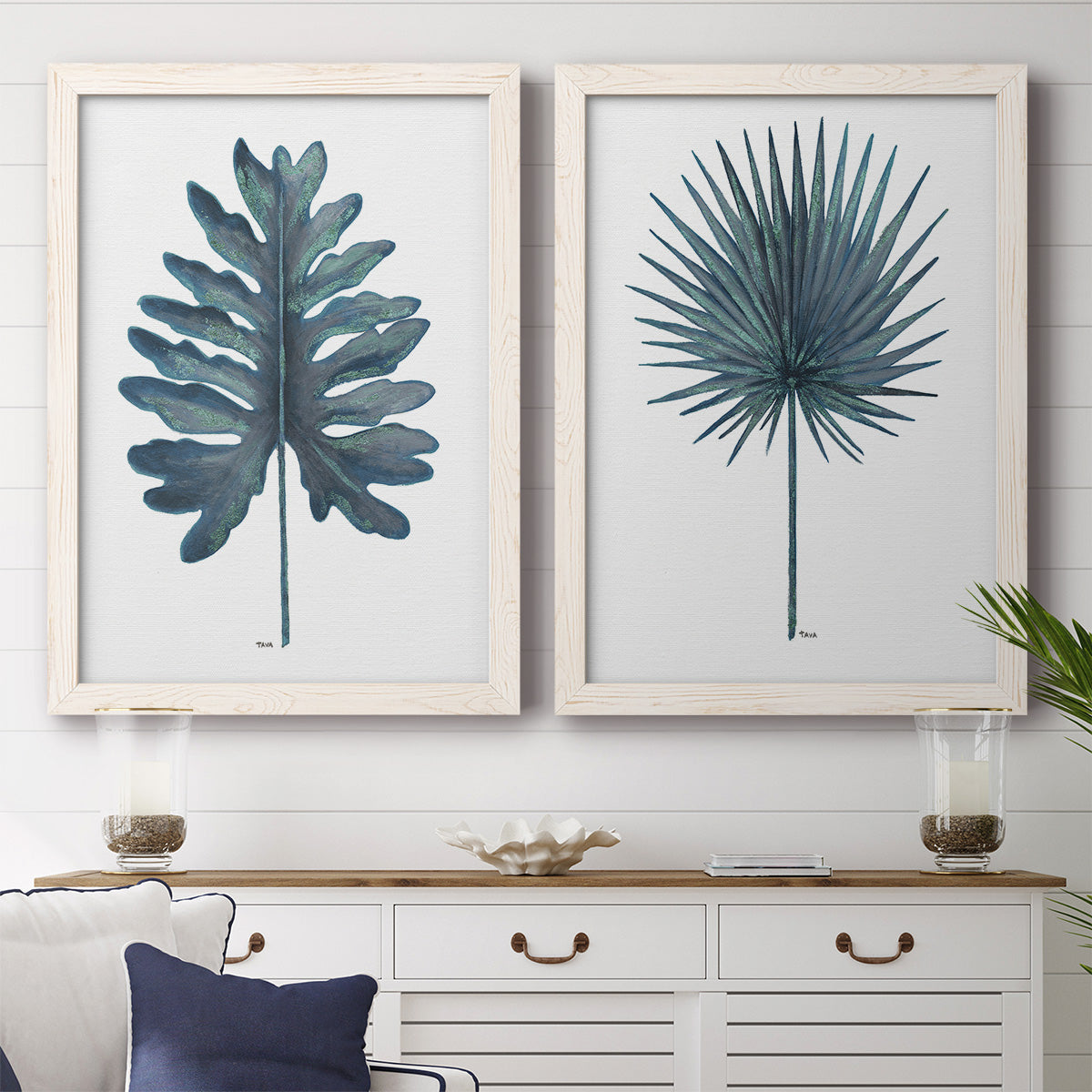 Set of two white barnwood framed canvas prints depicting a coordinated art pair of large blue-green tropical leaves rendered as modern botanical illustrations above a dining room sideboard.