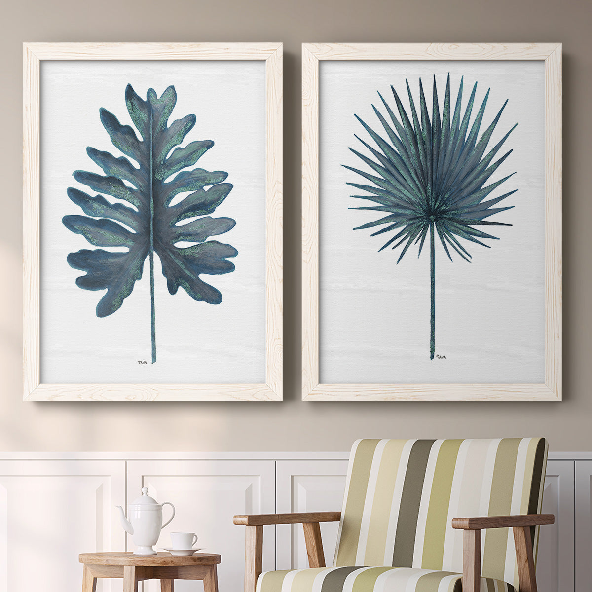 Set of two white barnwood framed canvas prints depicting two modern botanical illustrations featuring large blue-green tropical leaves above a sideboard in a cozy sitting room.