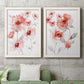 Set of two white barnwood framed canvas prints depicting a coordinated art pair of loose coral pink blossoms on slender gray stems rendered as airy contemporary watercolor florals above a sofa in a modern living room.