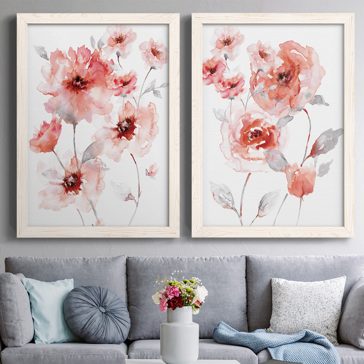 Set of two white barnwood framed canvas prints depicting paired airy contemporary watercolor florals with transparent petals, soft splashes, and abundant white space above a sofa in a contemporary living room.