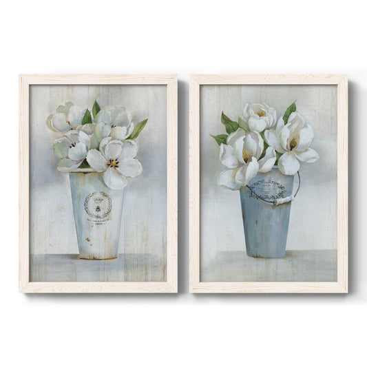 Set of two white barnwood framed canvas prints featuring two French-country floral still lifes featuring white blossoms arranged in weathered ceramic vases.