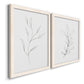 Angled view of a set of two white barnwood framed canvas prints featuring two minimalist botanical line drawings featuring single continuous-line leafy branches.