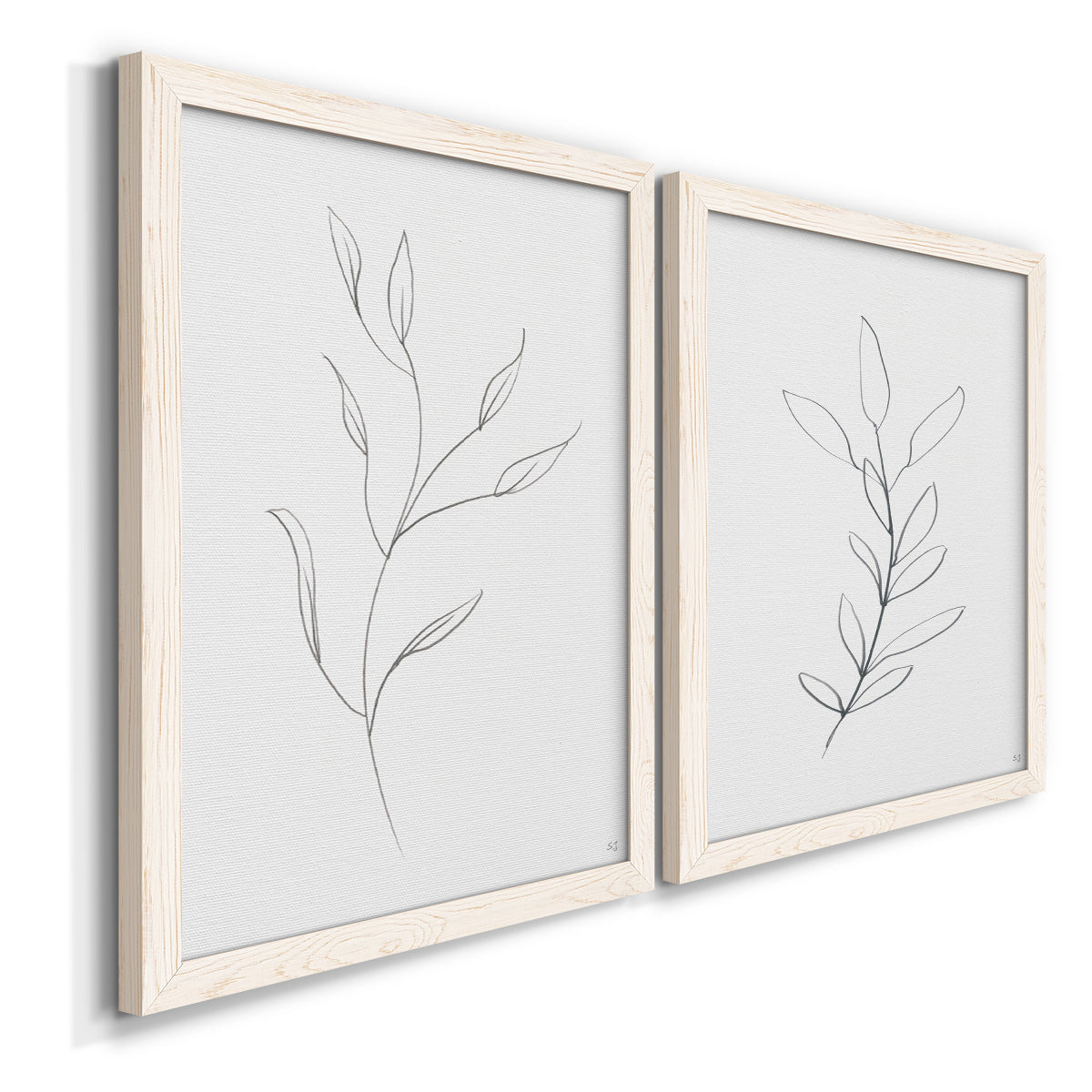 Angled view of a set of two white barnwood framed canvas prints featuring two minimalist botanical line drawings featuring single continuous-line leafy branches.