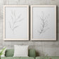 Set of two white barnwood framed canvas prints depicting a coordinated art pair of single continuous-line leafy branches rendered as minimalist botanical line drawings above a sofa in a modern living room.