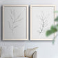 Set of two white barnwood framed canvas prints depicting thin gray contours, sparse stems, and clean white fields arranged across two complementary compositions above a sofa in a bright living space.