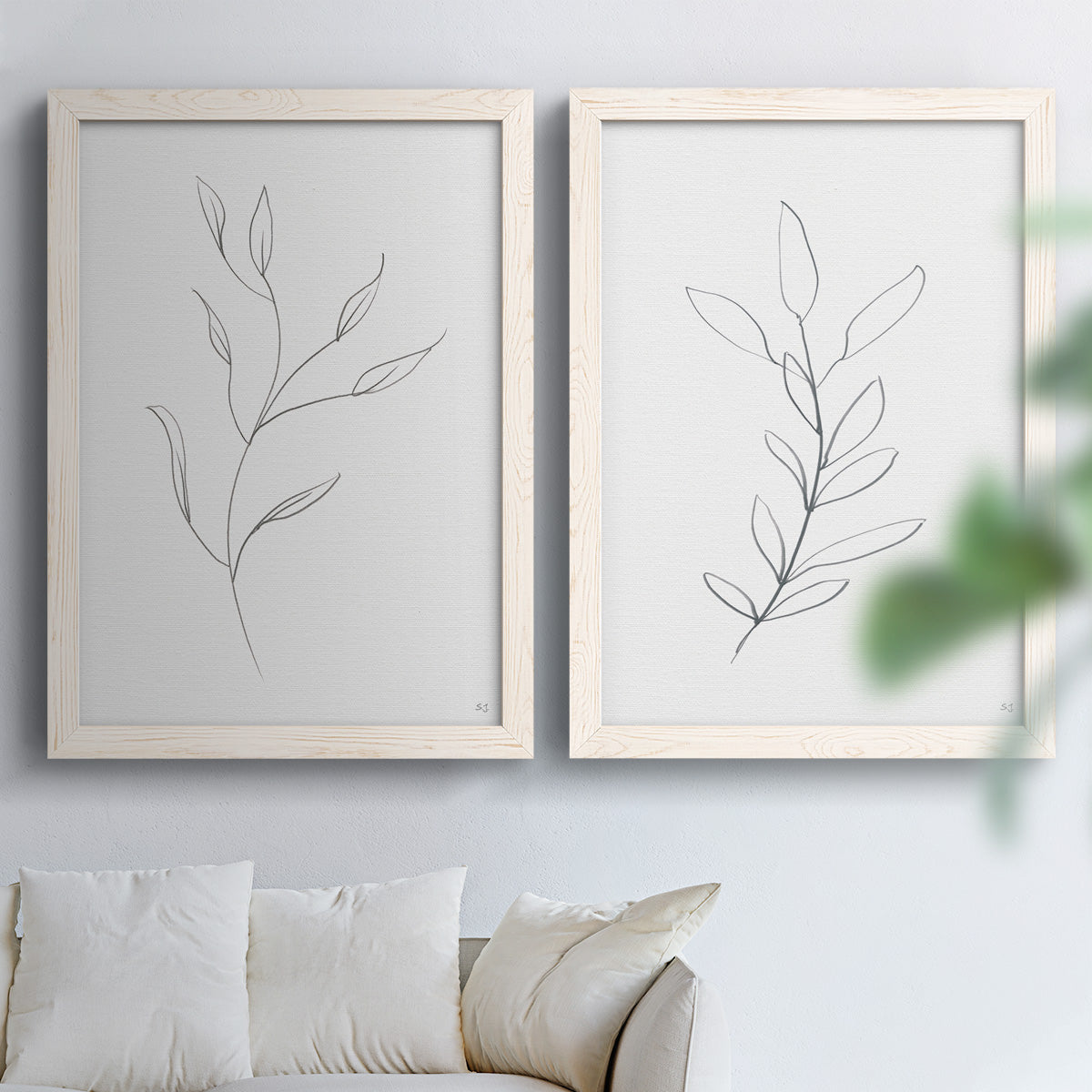 Set of two white barnwood framed canvas prints depicting thin gray contours, sparse stems, and clean white fields arranged across two complementary compositions above a sofa in a bright living space.