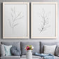 Set of two white barnwood framed canvas prints depicting paired minimalist botanical line drawings with thin gray contours, sparse stems, and clean white fields above a sofa in a contemporary living room.