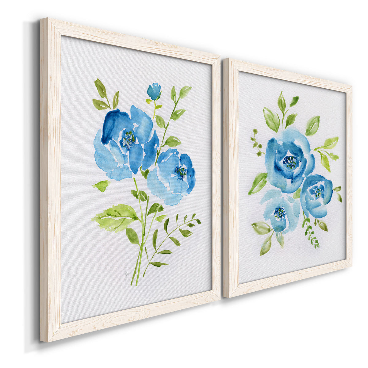 Angled view of a set of two white barnwood framed canvas prints featuring two contemporary botanical paintings featuring blue watercolor flowers with fresh green leaves.