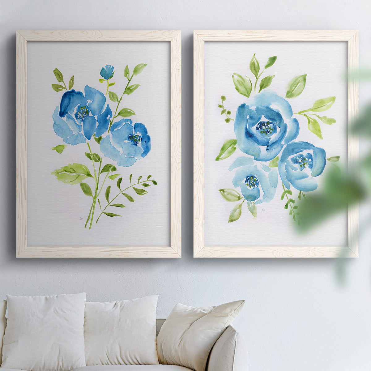 Set of two white barnwood framed canvas prints depicting open blossoms, delicate stems, and crisp white backgrounds arranged across two complementary compositions above a sofa in a bright living space.