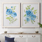 Set of two white barnwood framed canvas prints depicting a coordinated art pair of blue watercolor flowers with fresh green leaves rendered as contemporary botanical paintings above a dining room sideboard.
