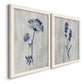 Angled view of a set of two white barnwood framed canvas prints featuring two rustic monochrome botanical paintings featuring blue wildflower stems on weathered neutral paper.