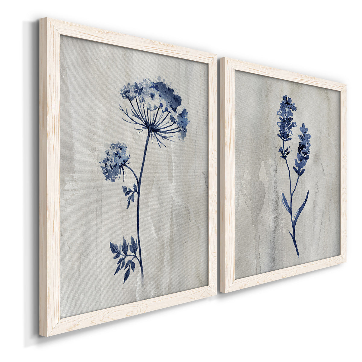 Angled view of a set of two white barnwood framed canvas prints featuring two rustic monochrome botanical paintings featuring blue wildflower stems on weathered neutral paper.