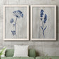 Set of two white barnwood framed canvas prints depicting a coordinated art pair of blue wildflower stems on weathered neutral paper rendered as rustic monochrome botanical paintings above a sofa in a modern living room.