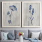 Set of two white barnwood framed canvas prints depicting paired rustic monochrome botanical paintings with indigo blossoms, thin stems, and softly distressed gray backgrounds above a sofa in a contemporary living room.