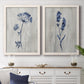Set of two white barnwood framed canvas prints depicting a coordinated art pair of blue wildflower stems on weathered neutral paper rendered as rustic monochrome botanical paintings above a dining room sideboard.