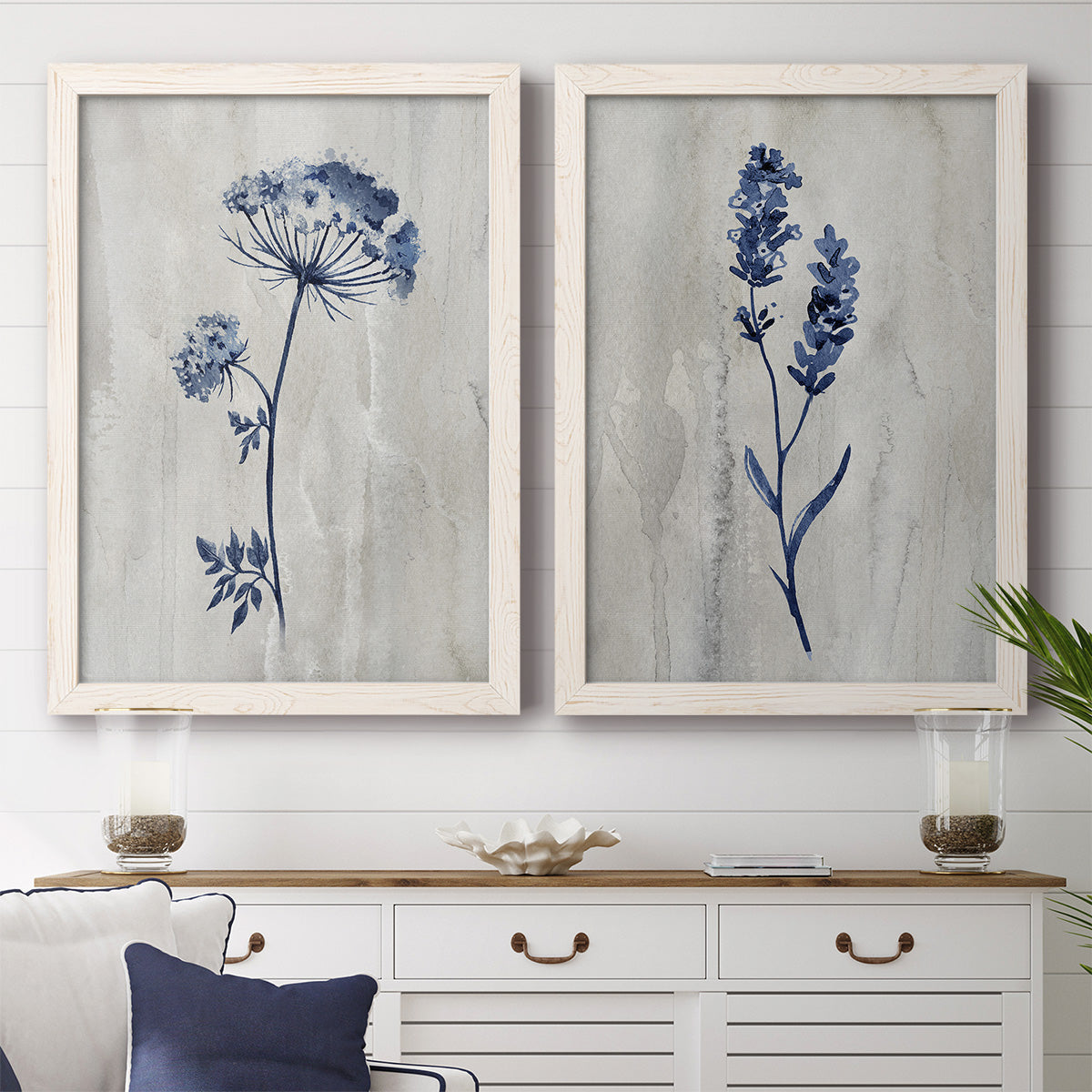 Set of two white barnwood framed canvas prints depicting a coordinated art pair of blue wildflower stems on weathered neutral paper rendered as rustic monochrome botanical paintings above a dining room sideboard.