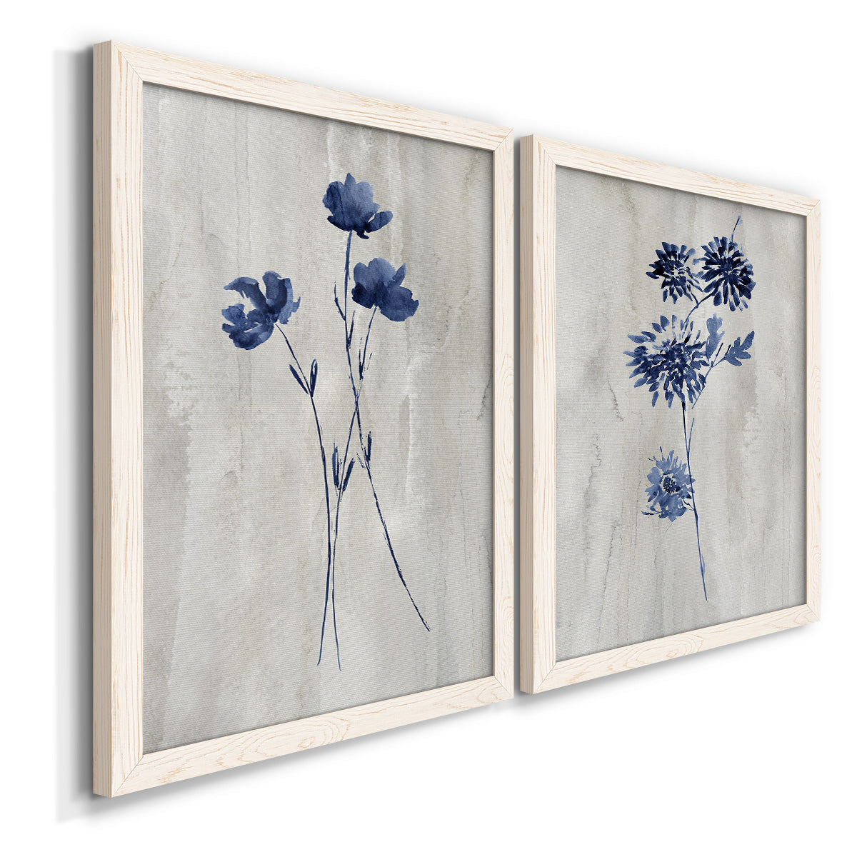 Angled view of a set of two white barnwood framed canvas prints featuring two rustic monochrome botanical paintings featuring blue wildflower stems on weathered neutral paper.