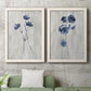 Set of two white barnwood framed canvas prints depicting a coordinated art pair of blue wildflower stems on weathered neutral paper rendered as rustic monochrome botanical paintings above a sofa in a modern living room.