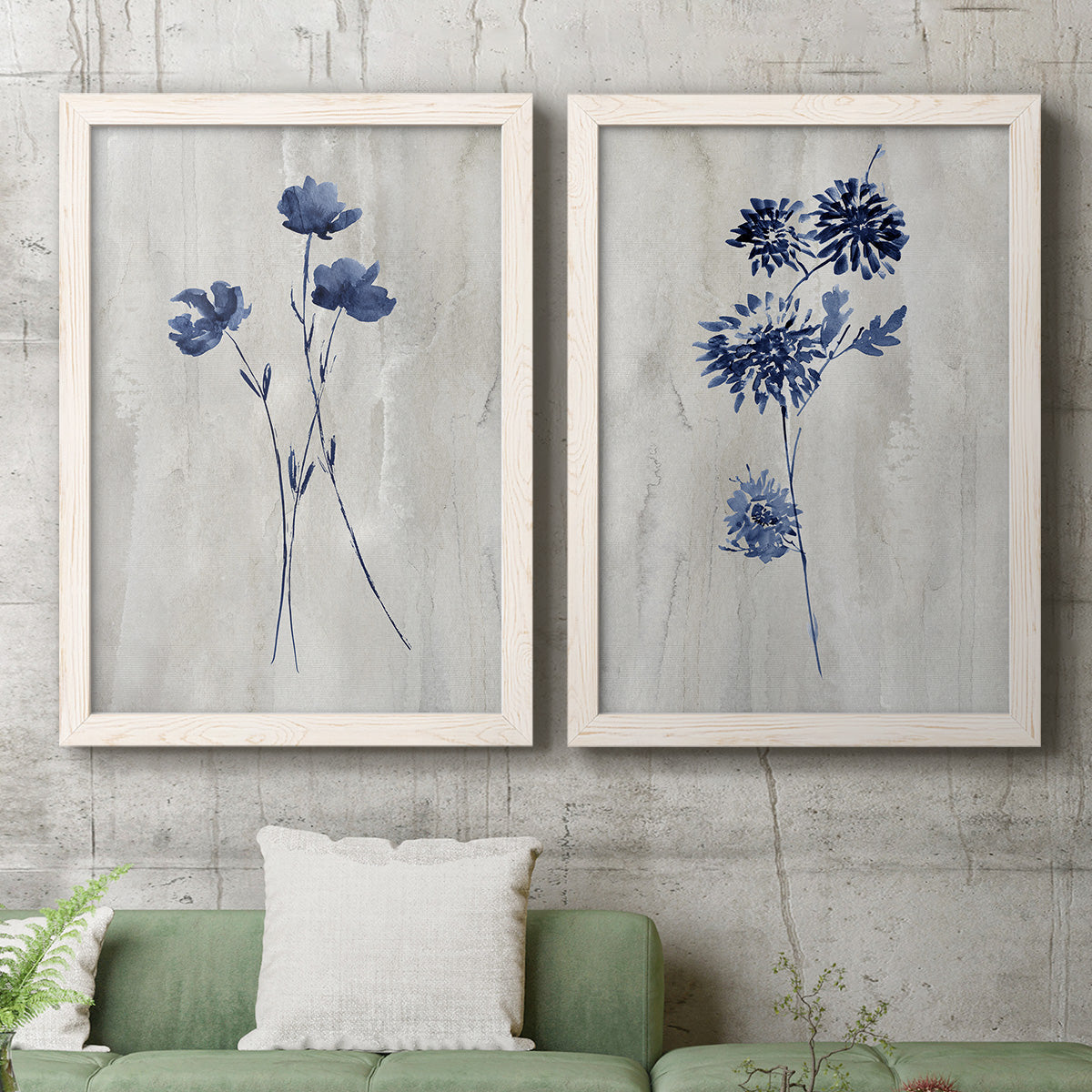 Set of two white barnwood framed canvas prints depicting a coordinated art pair of blue wildflower stems on weathered neutral paper rendered as rustic monochrome botanical paintings above a sofa in a modern living room.