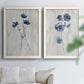 Set of two white barnwood framed canvas prints depicting indigo blossoms, thin stems, and softly distressed gray backgrounds arranged across two complementary compositions above a sofa in a bright living space.