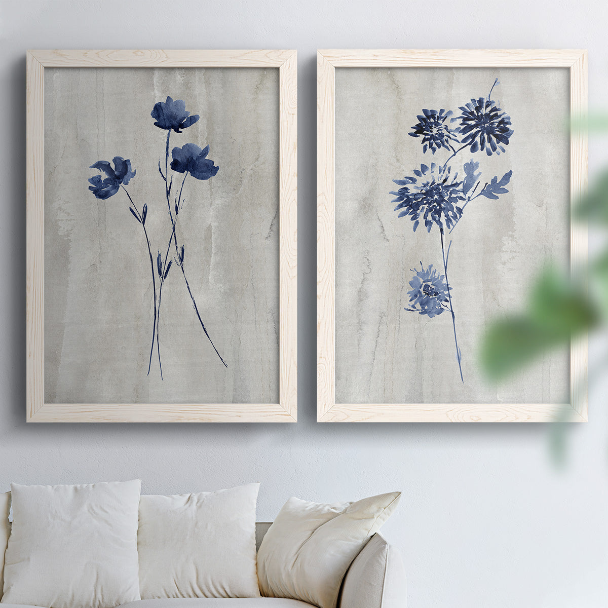 Set of two white barnwood framed canvas prints depicting indigo blossoms, thin stems, and softly distressed gray backgrounds arranged across two complementary compositions above a sofa in a bright living space.