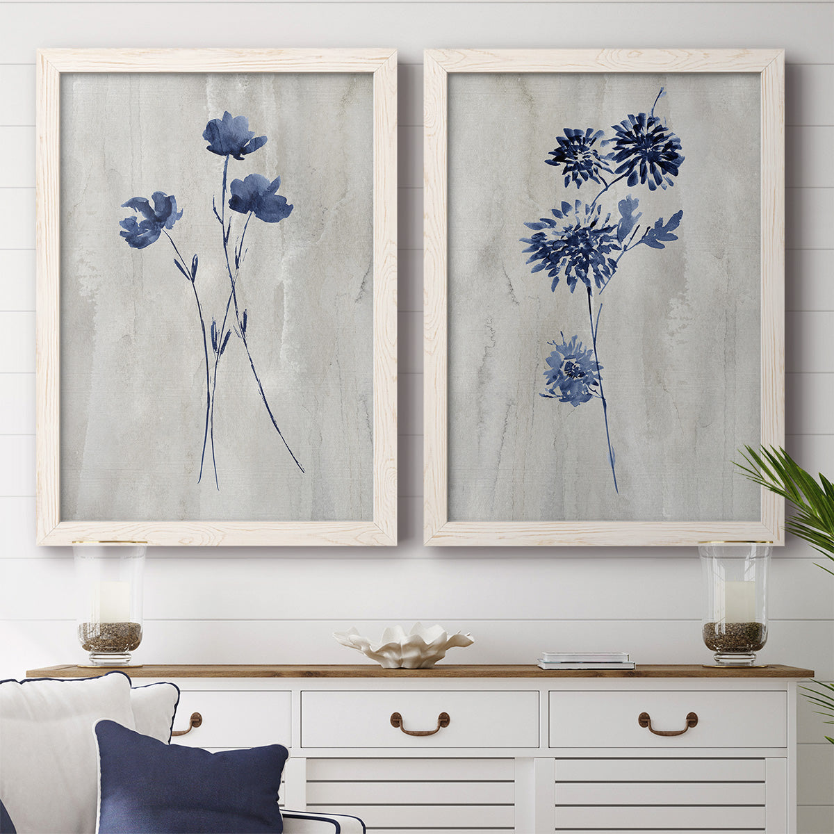 Set of two white barnwood framed canvas prints depicting a coordinated art pair of blue wildflower stems on weathered neutral paper rendered as rustic monochrome botanical paintings above a dining room sideboard.