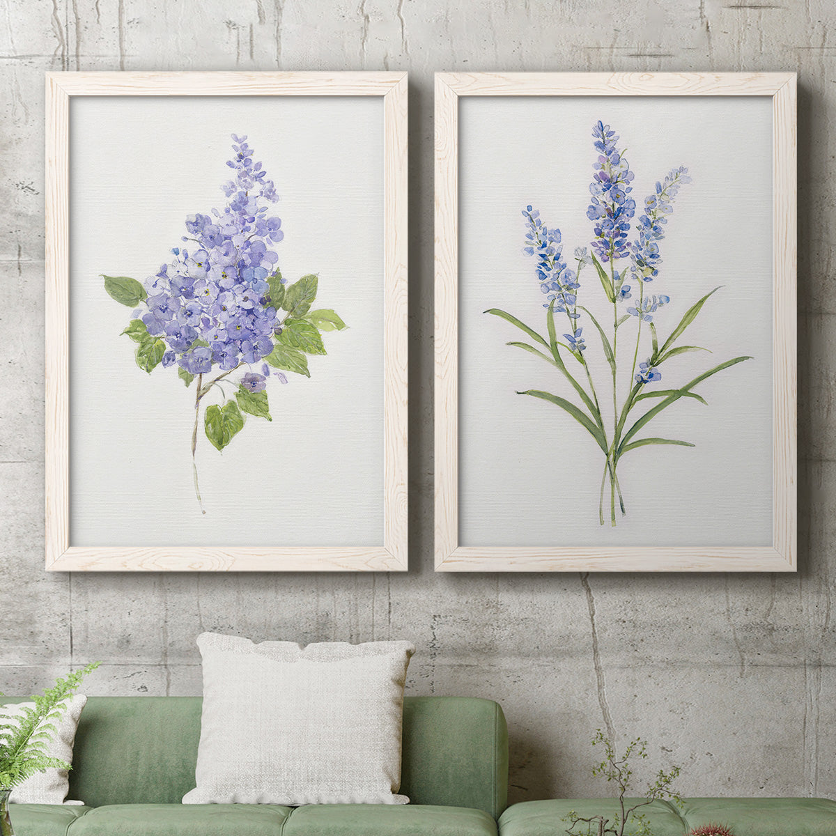 Set of two white barnwood framed canvas prints depicting a coordinated art pair of purple lilac and blue wildflower stems rendered as delicate watercolor botanical studies above a sofa in a modern living room.