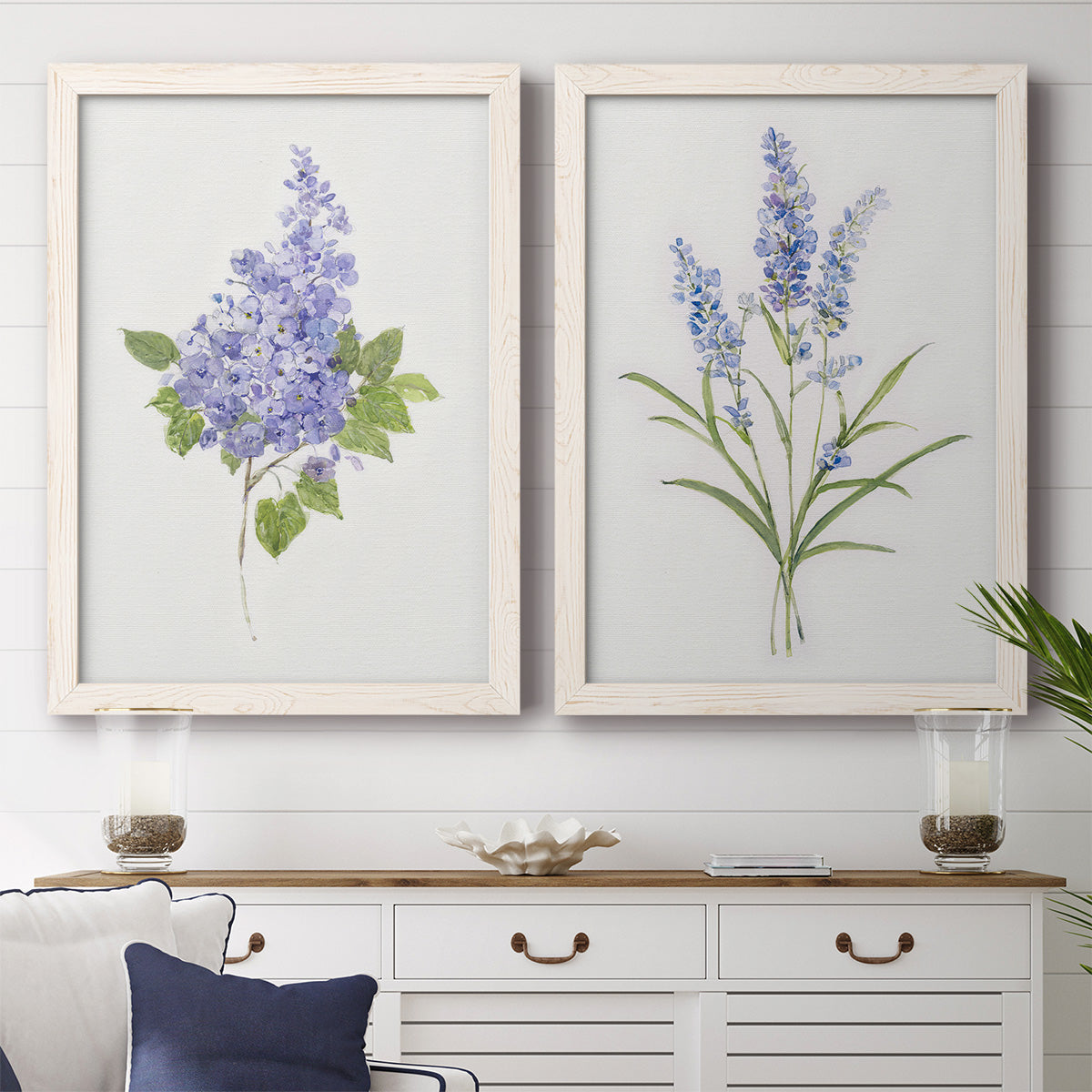 Set of two white barnwood framed canvas prints depicting a coordinated art pair of purple lilac and blue wildflower stems rendered as delicate watercolor botanical studies above a dining room sideboard.