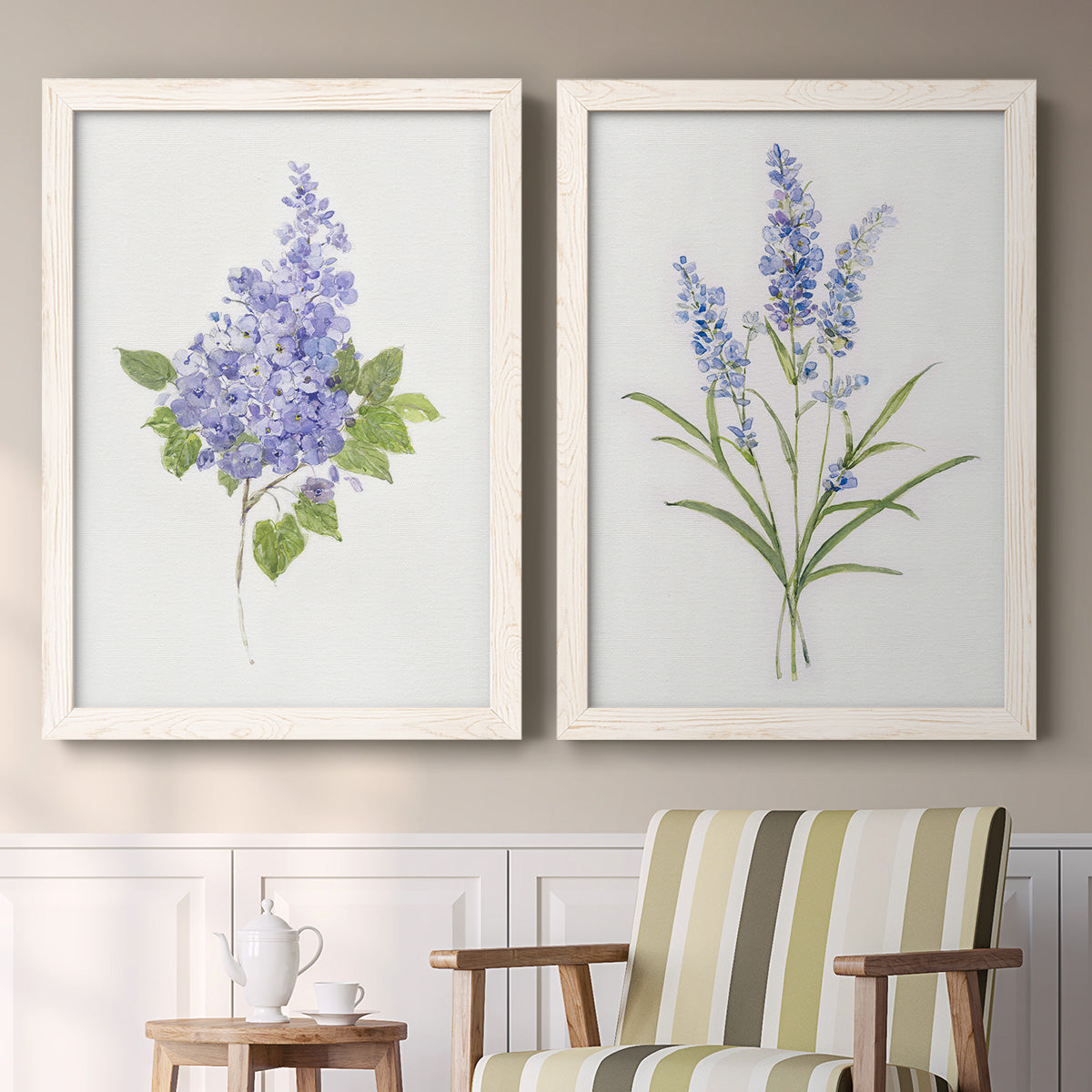 Set of two white barnwood framed canvas prints depicting two delicate watercolor botanical studies featuring purple lilac and blue wildflower stems above a sideboard in a cozy sitting room.