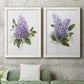 Set of two white barnwood framed canvas prints depicting a coordinated art pair of full purple lilac clusters with green leaves rendered as romantic traditional floral paintings above a sofa in a modern living room.