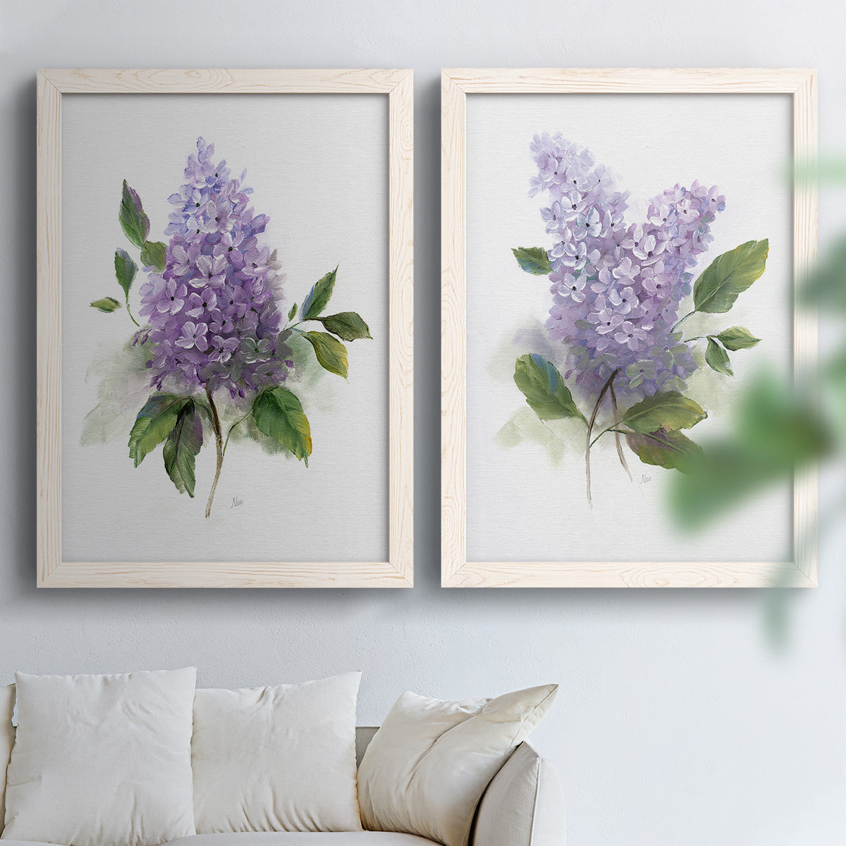 Set of two white barnwood framed canvas prints depicting layered lavender blossoms, broad foliage, and softly textured grounds arranged across two complementary compositions above a sofa in a bright living space.