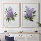 Set of two white barnwood framed canvas prints depicting a coordinated art pair of full purple lilac clusters with green leaves rendered as romantic traditional floral paintings above a dining room sideboard.