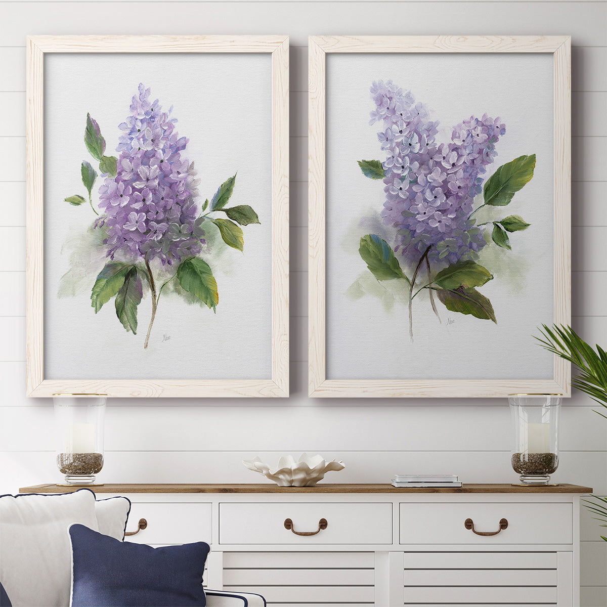 Set of two white barnwood framed canvas prints depicting a coordinated art pair of full purple lilac clusters with green leaves rendered as romantic traditional floral paintings above a dining room sideboard.