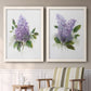 Set of two white barnwood framed canvas prints depicting two romantic traditional floral paintings featuring full purple lilac clusters with green leaves above a sideboard in a cozy sitting room.