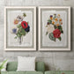 Set of two white barnwood framed canvas prints depicting a coordinated art pair of vintage mixed-flower bouquets on distressed paper rendered as traditional botanical collage prints above a sofa in a modern living room.