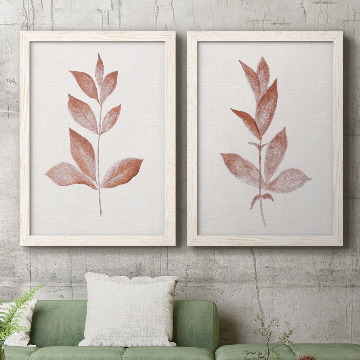 Set of two white barnwood framed canvas prints depicting a coordinated art pair of single rust-red leafy stems rendered as minimalist botanical prints above a sofa in a modern living room.