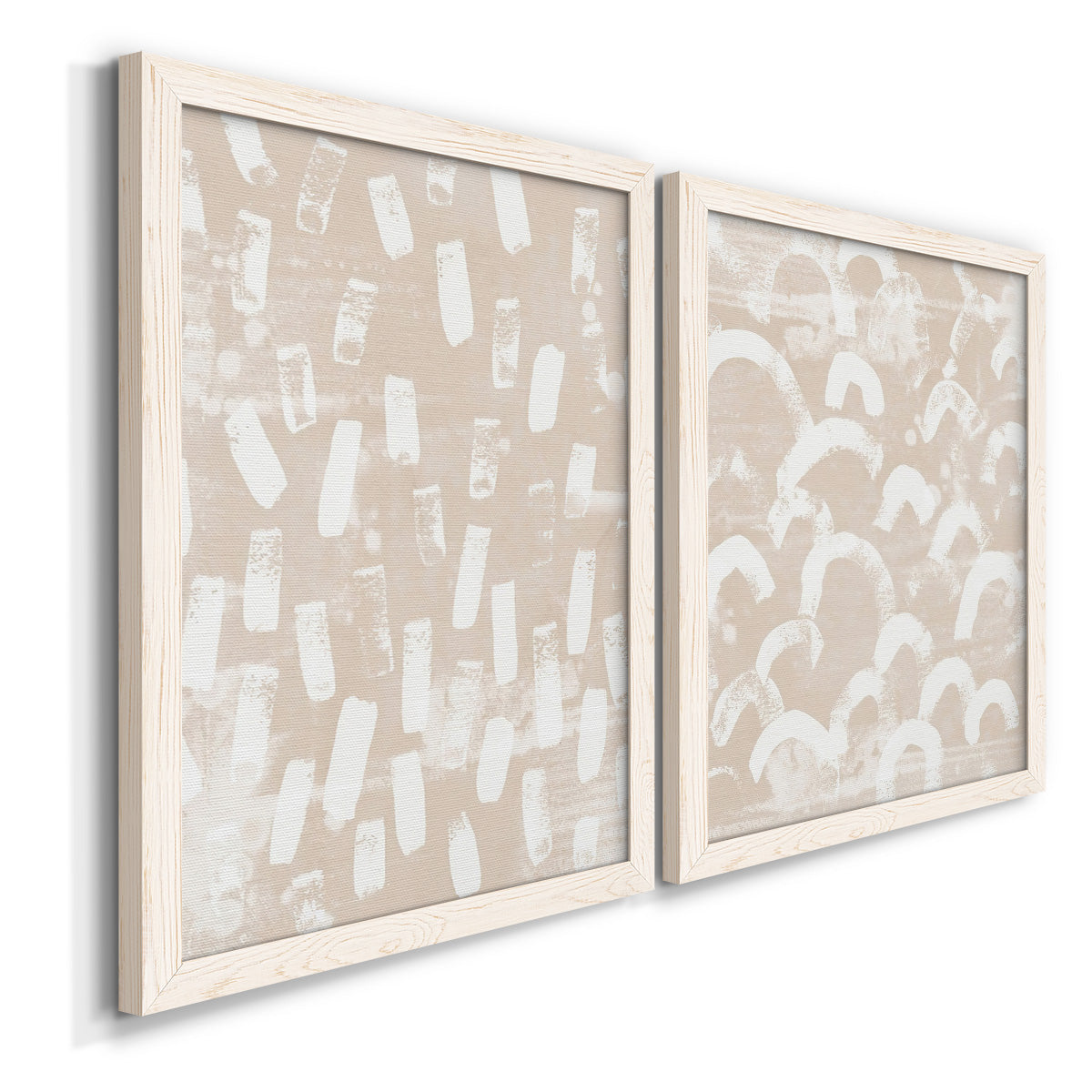 Angled view of a set of two white barnwood framed canvas prints featuring two tribal-inspired pattern abstracts featuring white hand-painted dashes arcs and chevrons.