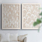 Set of two white barnwood framed canvas prints depicting repeating marks, warm beige grounds, and block-print texture arranged across two complementary compositions above a sofa in a bright living space.