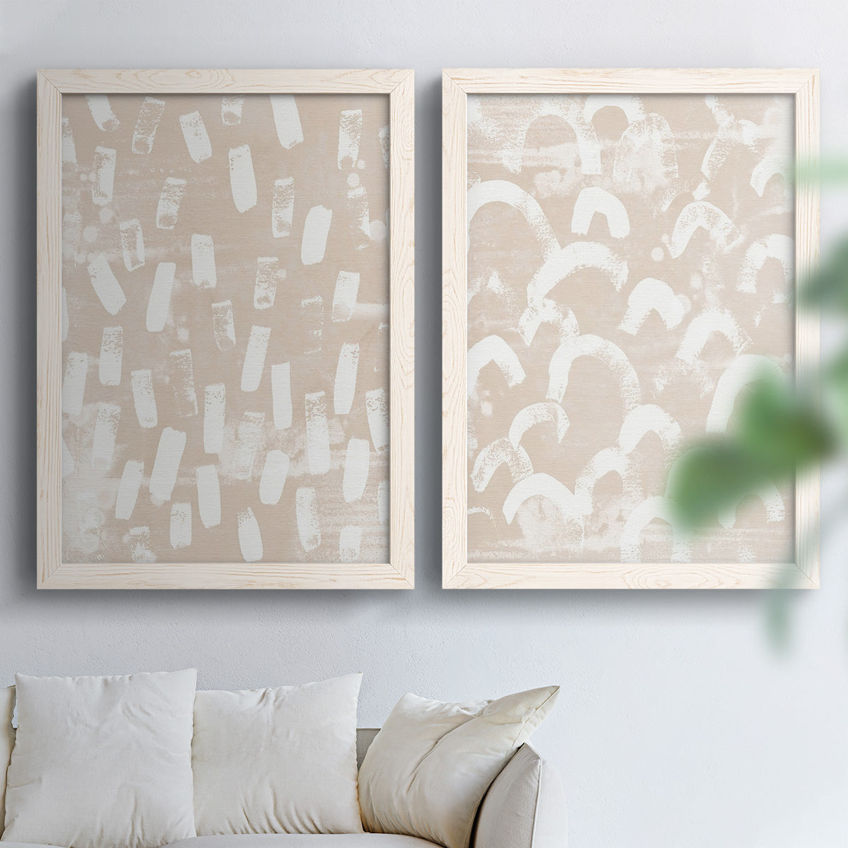Set of two white barnwood framed canvas prints depicting repeating marks, warm beige grounds, and block-print texture arranged across two complementary compositions above a sofa in a bright living space.