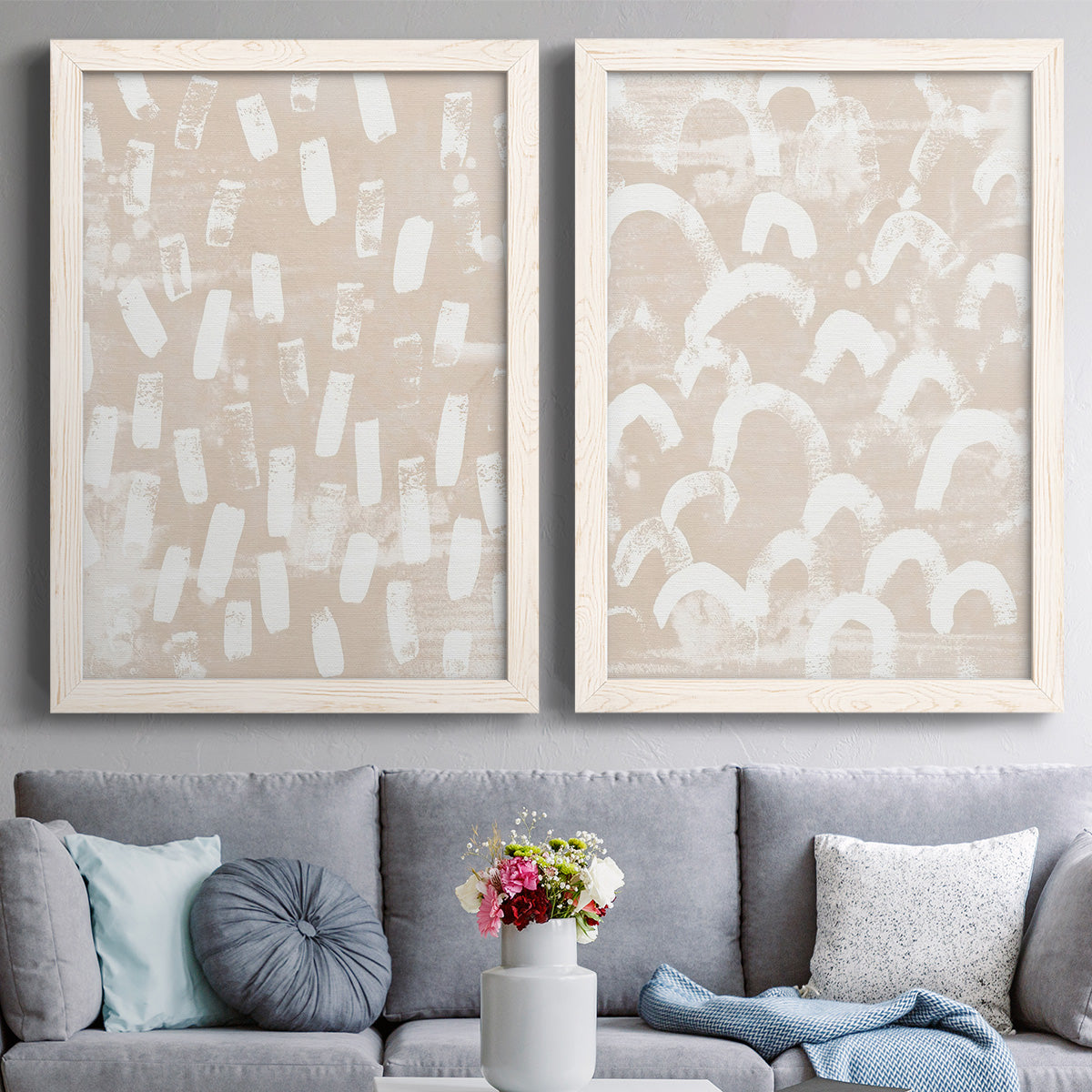 Set of two white barnwood framed canvas prints depicting paired tribal-inspired pattern abstracts with repeating marks, warm beige grounds, and block-print texture above a sofa in a contemporary living room.