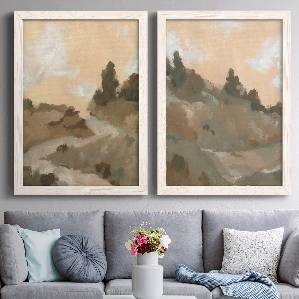 Set of two white barnwood framed canvas prints depicting paired minimalist watercolor landscapes with layered ridges, soft earth tones, and hazy cream skies above a sofa in a contemporary living room.