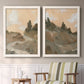 Set of two white barnwood framed canvas prints depicting two minimalist watercolor landscapes featuring misty brown hills and winding mountain paths above a sideboard in a cozy sitting room.