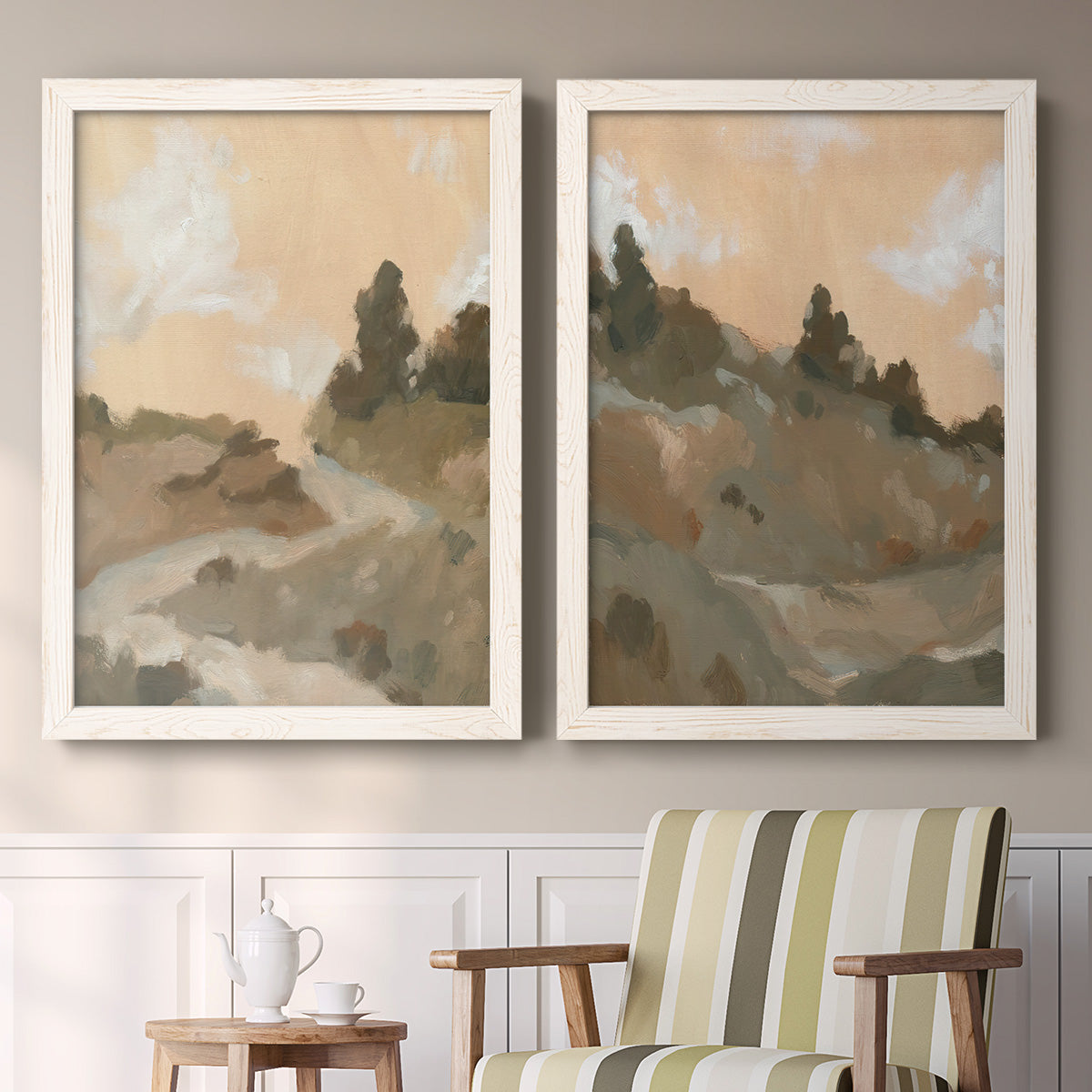 Set of two white barnwood framed canvas prints depicting two minimalist watercolor landscapes featuring misty brown hills and winding mountain paths above a sideboard in a cozy sitting room.