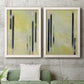 Set of two white barnwood framed canvas prints depicting a coordinated art pair of vertical black gray and olive bars rendered as minimalist architectural abstracts above a sofa in a modern living room.