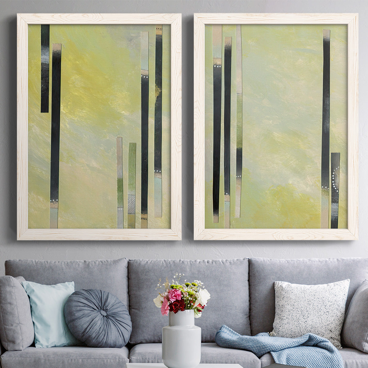 Set of two white barnwood framed canvas prints depicting paired minimalist architectural abstracts with slender rectangular elements, pale yellow fields, and subtle layered texture above a sofa in a contemporary living room.