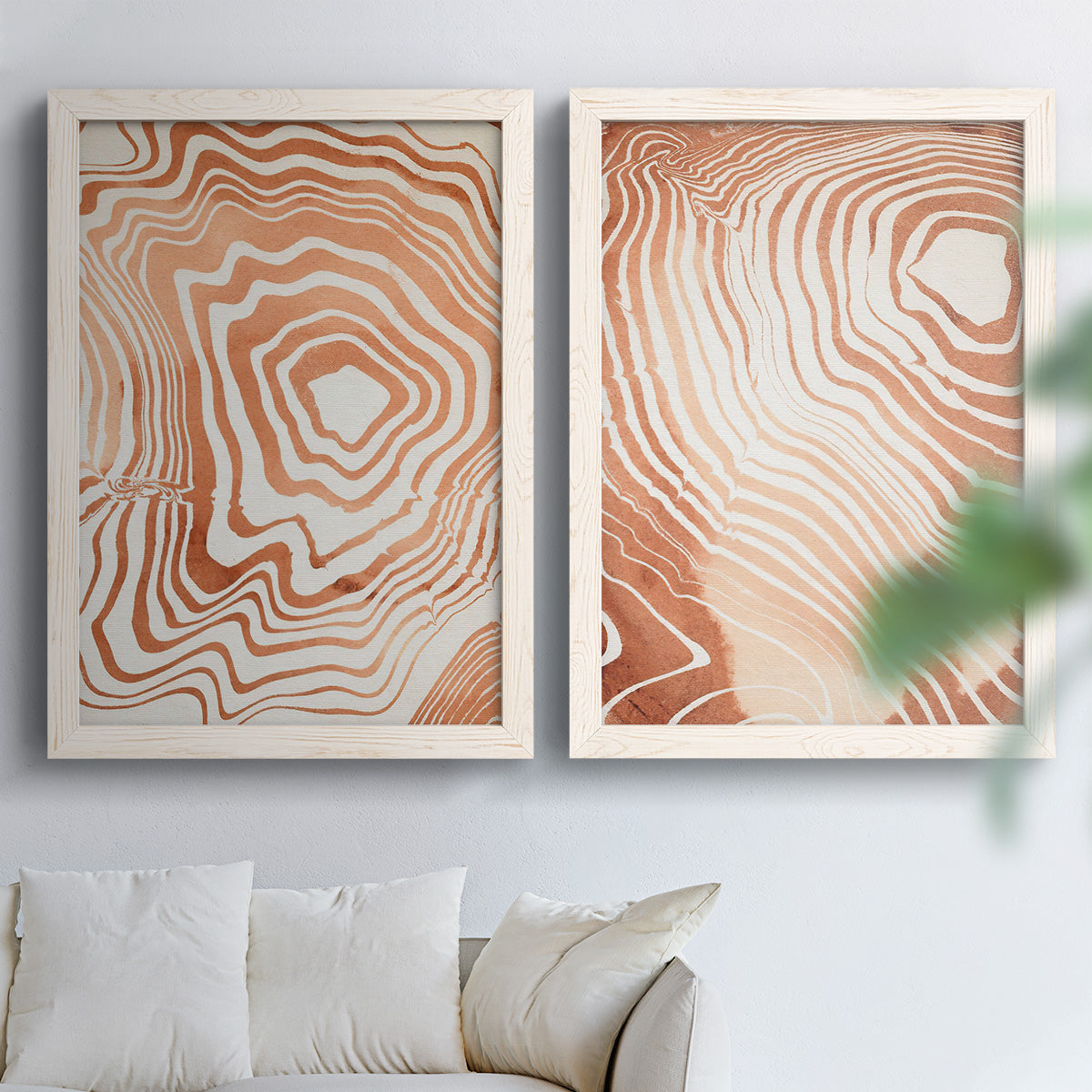 Set of two white barnwood framed canvas prints depicting warm terracotta lines, cream negative space, and organic nested curves arranged across two complementary compositions above a sofa in a bright living space.