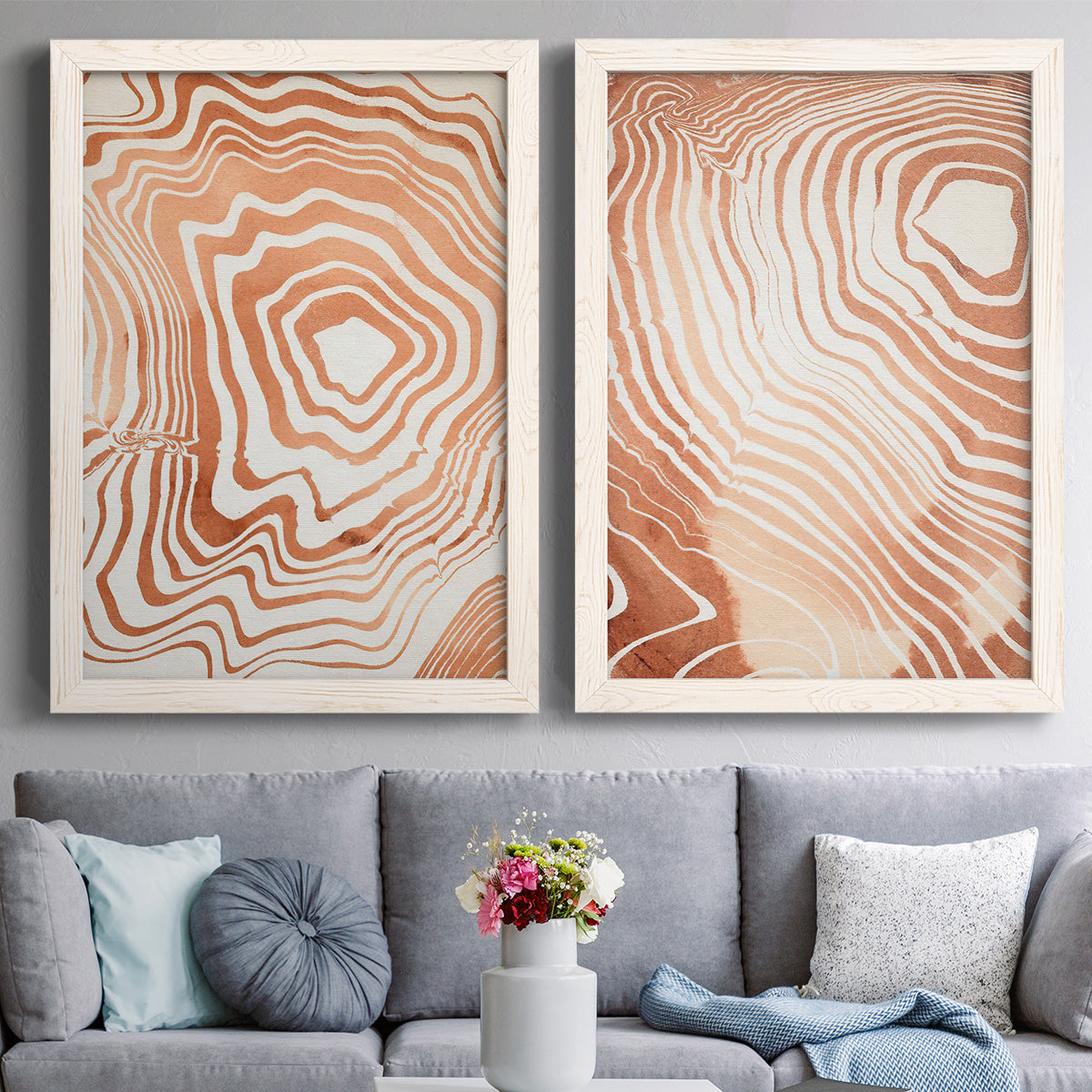 Set of two white barnwood framed canvas prints depicting paired minimalist marbled pattern abstracts with warm terracotta lines, cream negative space, and organic nested curves above a sofa in a contemporary living room.
