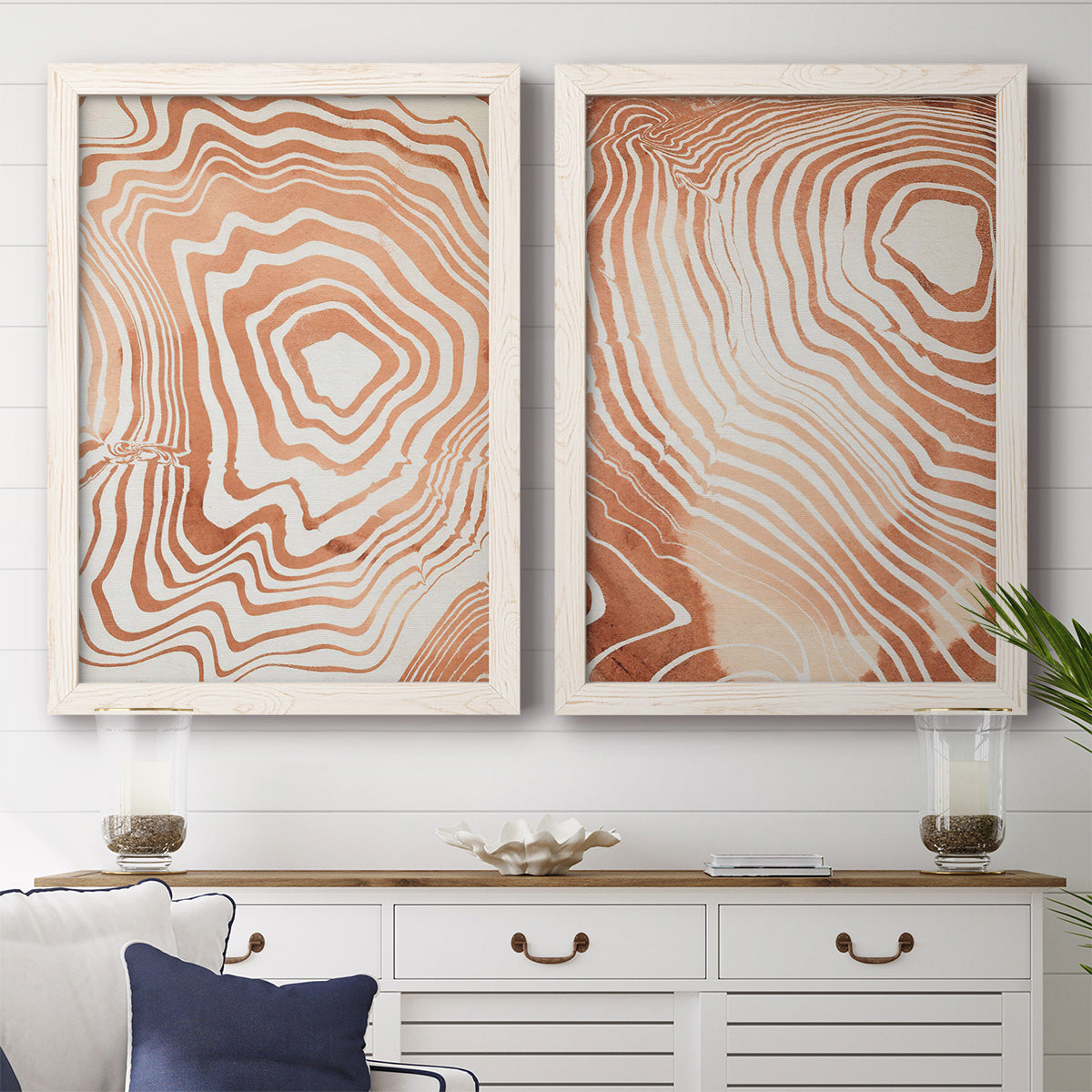 Set of two white barnwood framed canvas prints depicting a coordinated art pair of concentric wood-grain rings and rippling contour lines rendered as minimalist marbled pattern abstracts above a dining room sideboard.