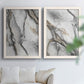 Set of two white barnwood framed canvas prints depicting fluid gray and black marbling with layered translucent forms and shimmering neutral details above a sofa in a bright living space.